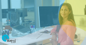 Woman smiling sat at a desk with a laptop and computer screen
