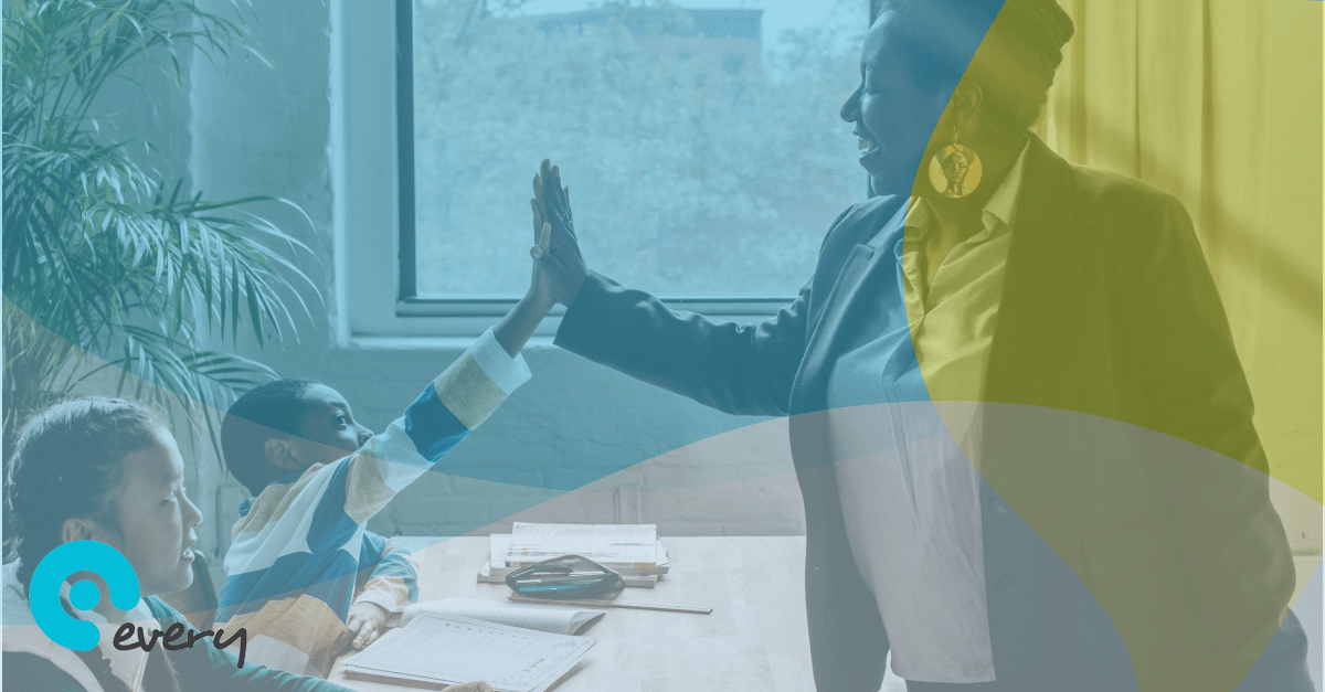Female teacher hi-fiving a student sat at their school desk next to another student