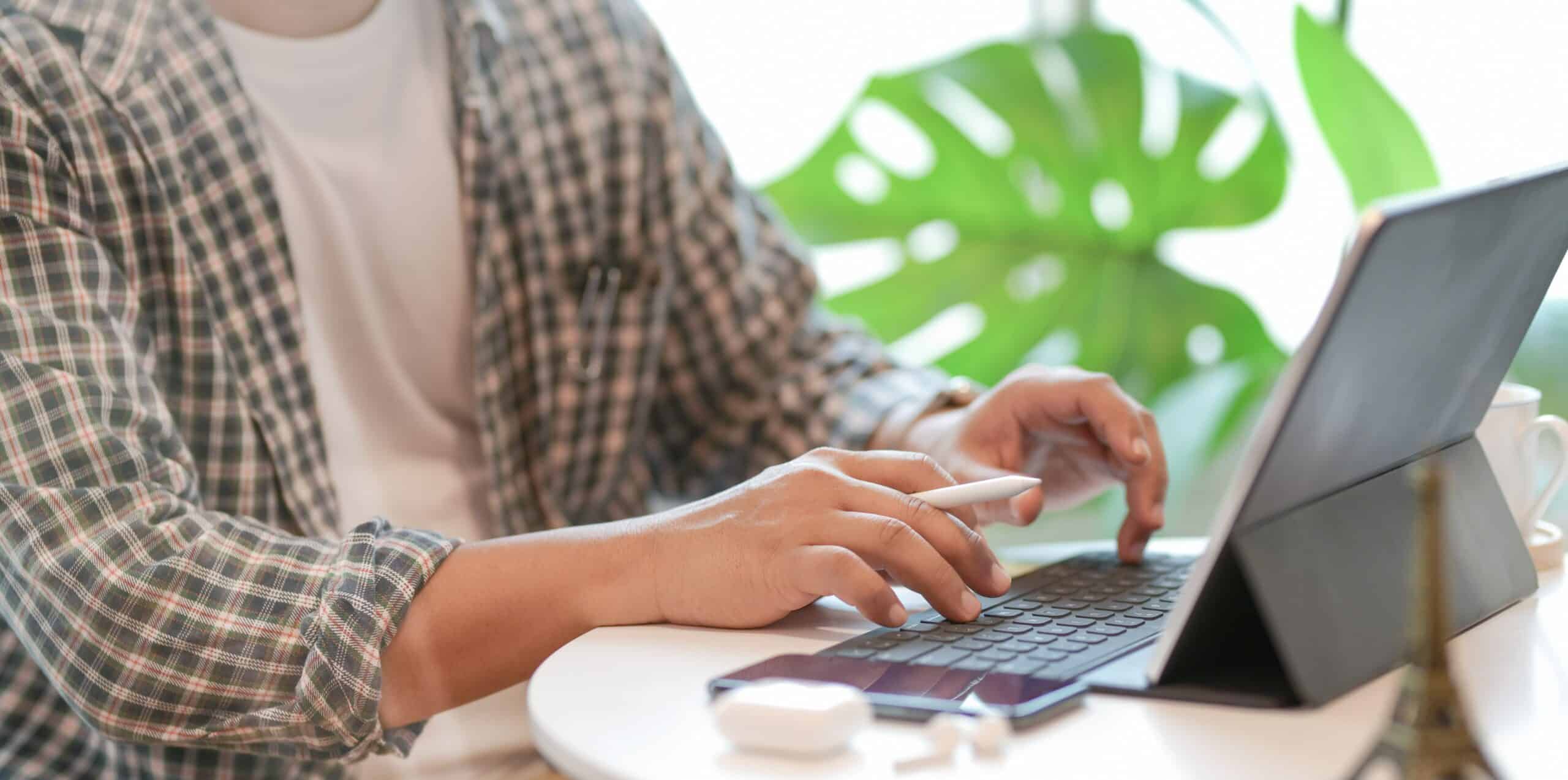 Person typing on laptop with plant in background